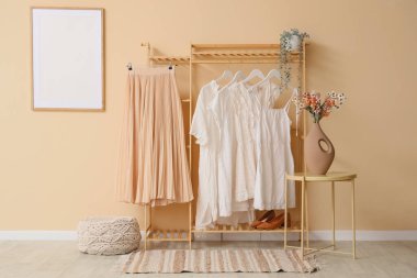 İç kısımda bej duvarın yanında şık kıyafetler var.