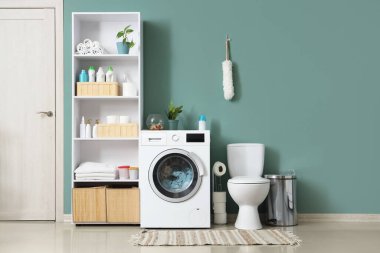 Çamaşır makinesi, klozet ve raf ünitesi olan bir çamaşırhane.