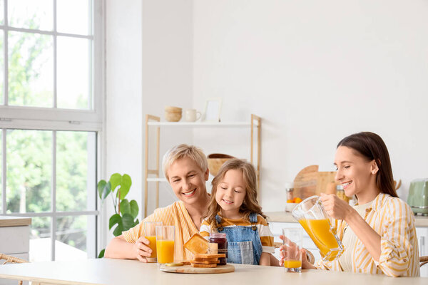 Маленькая девочка с матерью и бабушкой пьют сок за столом на кухне