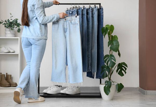 Женщина берет стильные джинсы из стойки в магазине одежды, вид сзади