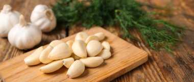 Tahta kesme tahtası taze sarımsak karanfilleri ve ahşap arka planda dereotu, yakın plan.