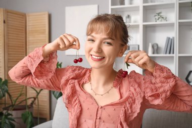 Oturma odasındaki kanepede oturan olgun kirazları olan güzel, mutlu genç bir kadın.