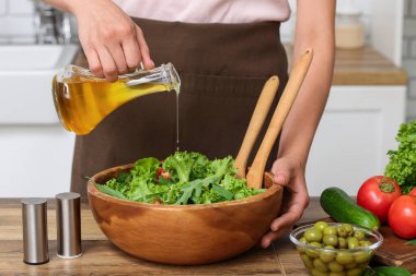 Mutfaktaki masada lezzetli salata ile zeytinyağı ekleyen bir kadın.