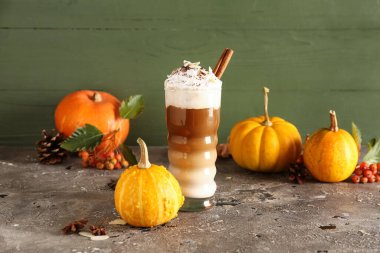 Yeşil duvarın yanındaki masada bir bardak tarçınlı ve bademli balkabaklı latte.