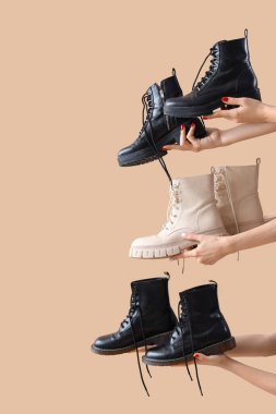 Bej arka planda farklı çizmeler tutan kadın eller.