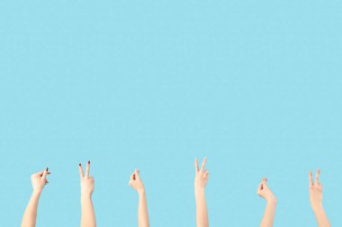 Kadın elleri barış jestleri gösteriyor ve mavi arka planda bir şey tutuyor.