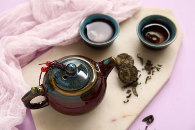 Çaydanlıklı mermer tepsi, bir fincan çay ve mor arkaplanda kurutulmuş çay.