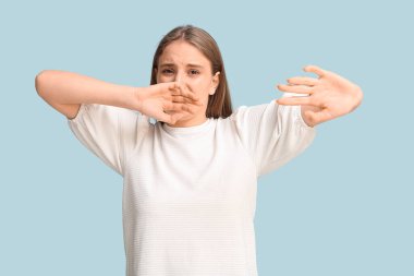 Genç bir kadın mavi arka planda korkunç bir koku hissediyor.