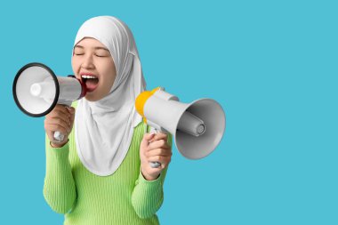 Genç Asyalı Müslüman kadın mavi arka planda megafonlara bağırıyor. Ulusal Duyulma Günü