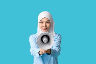 Mavi arka planda megafonu olan genç Asyalı Müslüman kadın. Ulusal Duyulma Günü