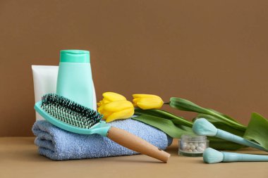 Havlu, makyaj ve kahverengi arka planda lale çiçekleri olan saç fırçaları.