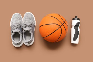 Gri spor ayakkabıları, basketbol ve spor şişesi kahverengi arka planda.