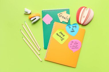 Planlar, not defterleri ve yeşil arka planda kırtasiye malzemesi olan yapışkan notlar. Yeni yıl hedefleri kavramı