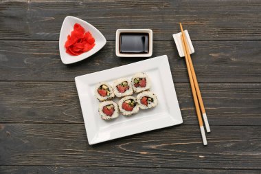 Soya soslu lezzetli suşi ruloları, yemek çubukları ve ahşap arka planda marine edilmiş zencefil.