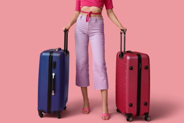 Pembe arka planda bavulları olan genç bir kadın. Seyahat kavramı