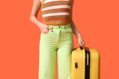 Turuncu arka planda sarı valizli genç bir kadın. Seyahat kavramı