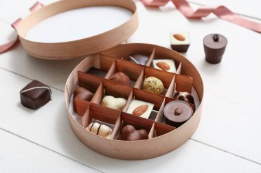 Beyaz ahşap arka planda lezzetli çikolata şekerleri olan kutu, yakın plan.