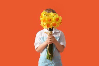 Cute little happy boy with bouquet of beautiful narcissus on orange background