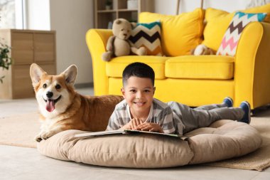 Little happy Asian boy reading book with cute Corgi dog at home