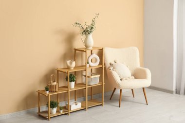 Vazodaki güzel çiçek açan dallar raf ünitesinde ev bitkileri ve bej duvarın yanındaki koltuk.