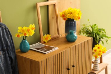 Güzel nergis çiçekleri, salondaki çekmecelerin üzerindeki çerçeve ve dergi