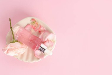 Pembe arka planda kozmetik yağı, gül ve taç yaprakları olan kompozisyon