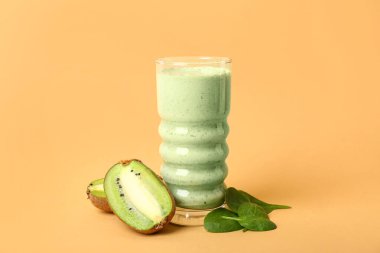 Bir bardak taze ıspanaklı smoothie ve sarı arka planda kivi.