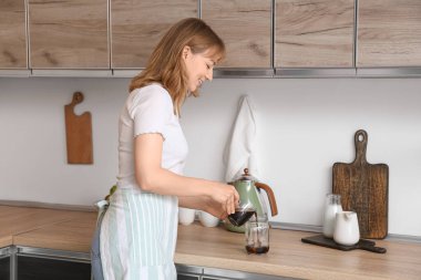 Genç bir kadın mutfaktaki buzla bardağa kahve dolduruyor.