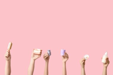 Pembe arka planda sünger fırçası, sabun çubuğu, mum, çiçek, bir şişe kozmetik ürünü ve deniz tuzu olan kadın eller.