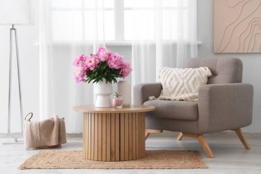 Sehpanın üzerinde pembe şakayık çiçekleri olan vazo şık oturma odasındaki yumuşak koltuğun yanında.