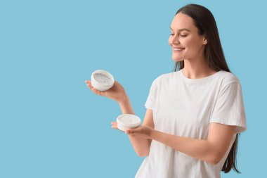 Mavi arka planda diş pudrası dolu kavanozları olan genç bir kadın.