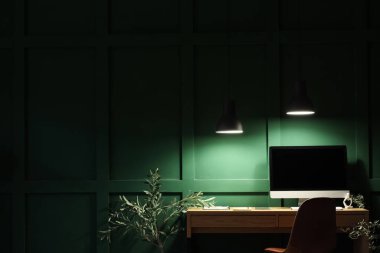 Geceleri ofisteki yeşil duvarın yanında modern bilgisayarlı şık bir iş yeri.