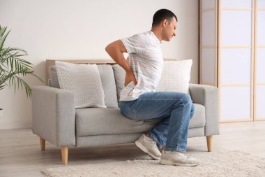 Evdeki kanepede sırt ağrısı çeken genç bir adam.