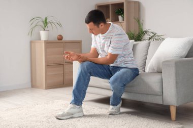 Evdeki kanepede bileğindeki ağrıdan muzdarip genç bir adam.