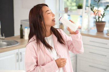 Güzel genç Asyalı kadın evde lezzetli yoğurt içiyor.