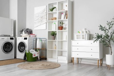 Çamaşır makinesi, raf ünitesi ve çekmeceleri olan hafif bir banyo.