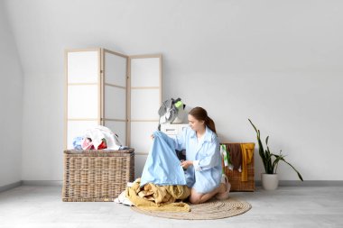 Çamaşır odasında çamaşır makinesinin yanında kirli çamaşırları sıralayan genç bir kadın.