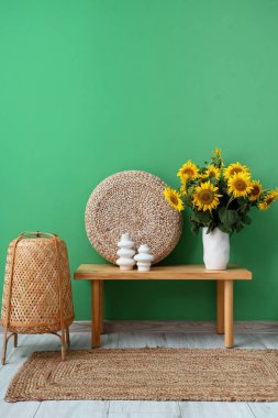 Hasır lambalı şık bir oda ve yeşil duvarın yanında bir vazo ayçiçeği buketi
