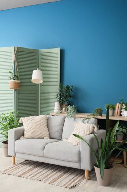 Kanepe, lamba, katlanan ekran ve oturma odasının içindeki bitkiler.