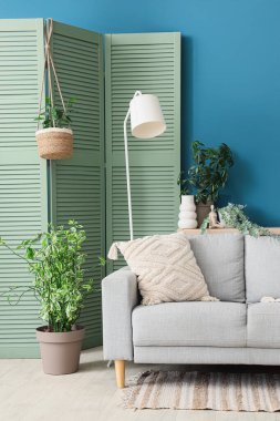 Kanepe, lamba, katlanan ekran ve oturma odasının içindeki bitkiler.