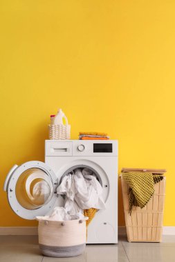 Çamaşır ve sepetli çamaşır makinesi sarı duvarın yanında.