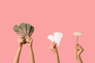 Yeniden kullanılabilir pedleri ve pembe arka planda çiçekleri olan kadın elleri