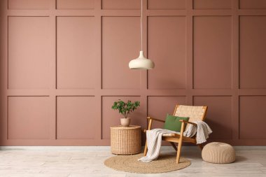 Yumuşak puflu şık koltuk ve kahverengi duvarın yanındaki hasır masa.