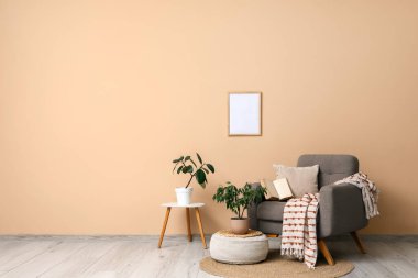 Rahat gri koltuk, yumuşak puf ve bej duvarın yanında bitkiler.