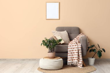 Yumuşak puflu şık gri koltuk ve bej duvarın yanında bitkiler.