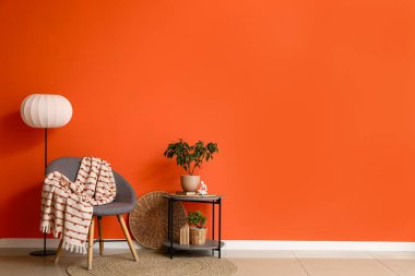 Turuncu duvarın yanında masa ve zemin lambası olan rahat gri koltuk.