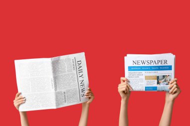 Kırmızı arka planda gazeteleri olan kadın eller