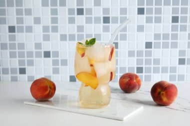 Şeftali dilimli bir bardak içki, buz küpleri ve mermer masa üzerindeki nane yaprakları fayans duvarına karşı.