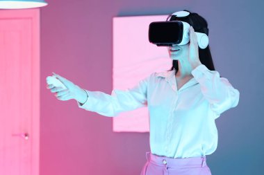 Modern sanat galerisinde VR gözlükleri ve kontrolörü olan genç bir kadın.