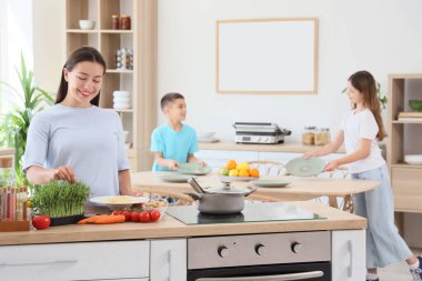 Genç anne ve çocukları mutfakta yemek masası hazırlıyorlar.